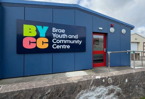 Blue building with a sign that reads “BYCC Brae Youth and Community Centre” and a red door.