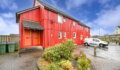 A bright red wooden-clad two-storey house with orange doors and a white van parked beside it, under a partly cloudy blue sky.