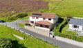 Aerial view of a cream two-storey house with a terracotta tiled roof, solar panels, and a red-framed conservatory, set on a hillside beside