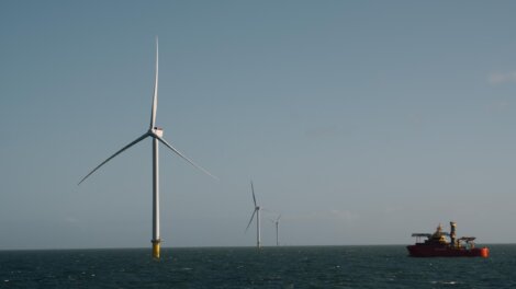 Offshore wind turbines standing in the sea near a red service vessel.