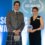 A smiling man in a grey Highland jacket and tartan kilt stands beside a woman in a black sleeveless outfit holding a blue-and-white award