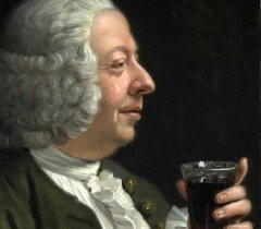 A man with white curly hair and 18th-century clothing holds a glass of dark beverage, looking at it with a slight smile against a dark background.
